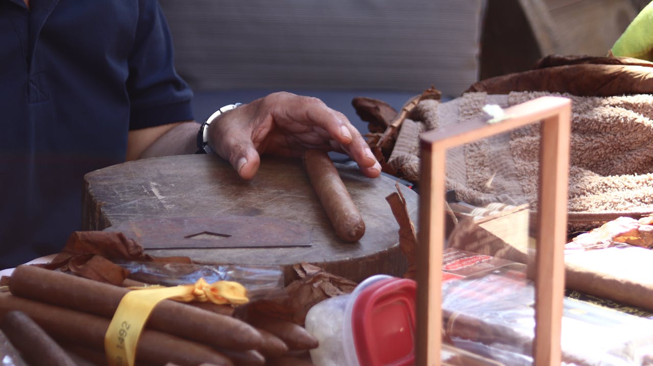 Detailed view of cigar crafting with a hand positioned on a table, depicting the art and tradition of cigar making.