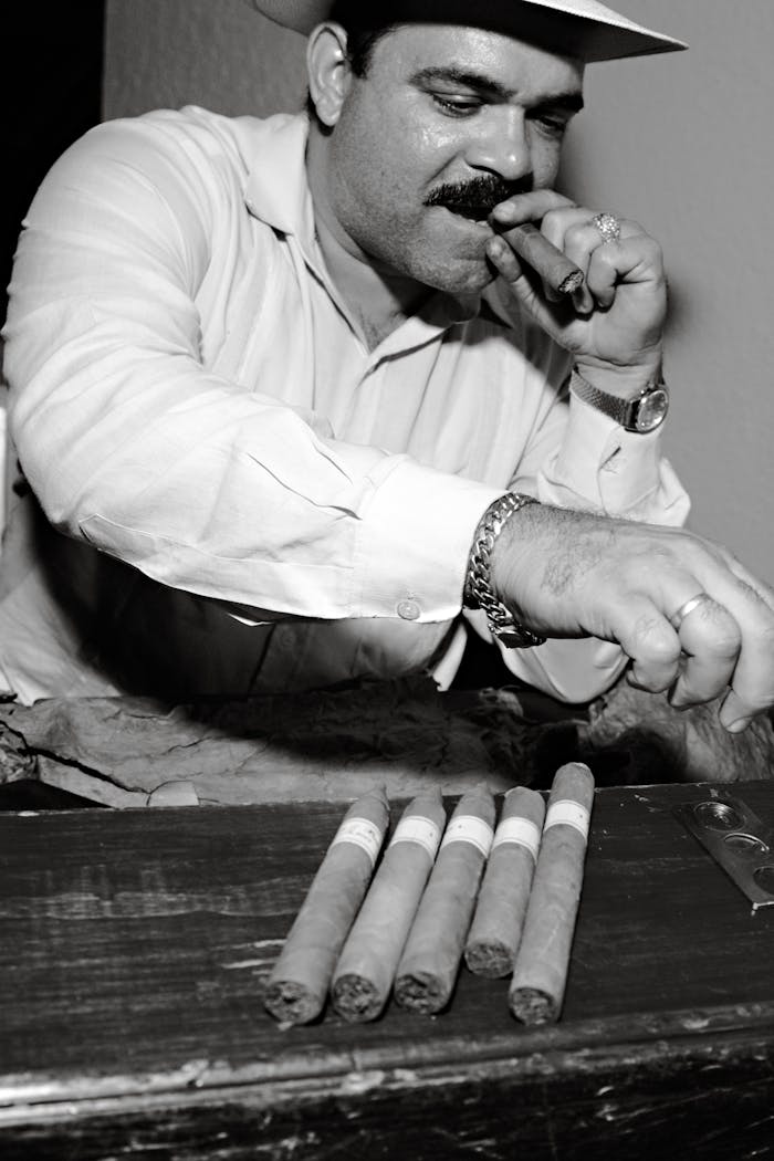 about-05 Cuban cigar maker savoring a cigar while showcasing freshly rolled cigars in Cuba.
